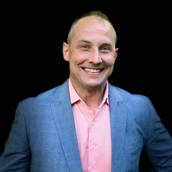 Man wearing a blue suit and pink undershirt on a black background