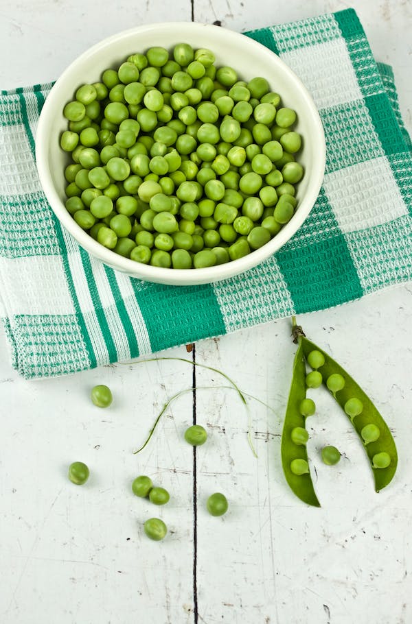 Bowl of peas on a plaid green cloth laid on a white wood table