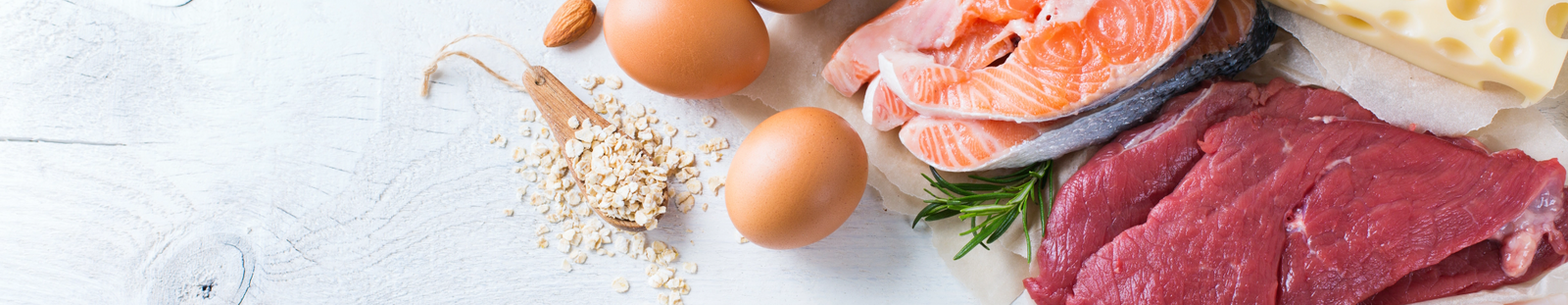 Fresh fish, red meat, eggs, cheese, and oats on a countertop