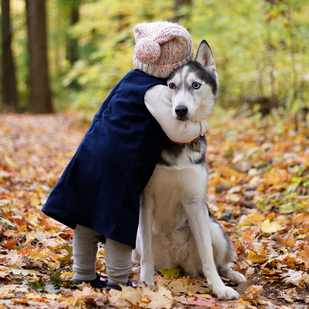 Toddler leaning in to hug a sitting husky in the woods